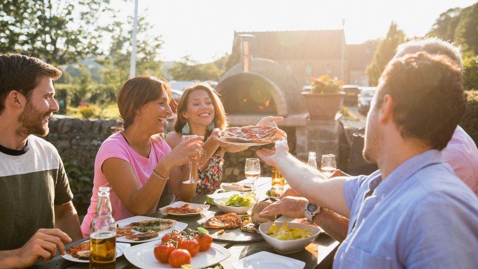 Friends sharing pizza and salad together outdoors in warm evening light