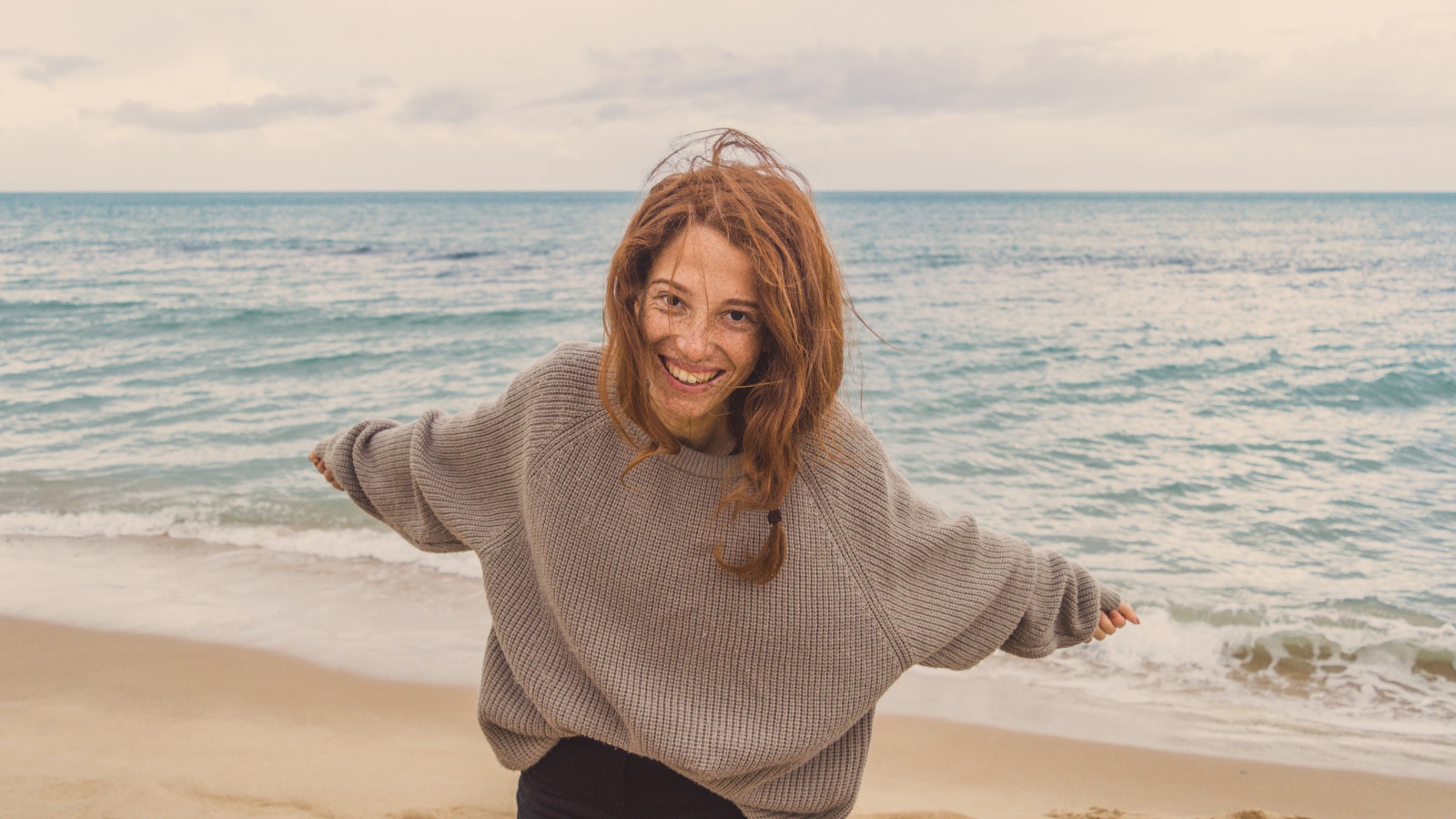 A smiling woman moving freely on a beach beside the sea