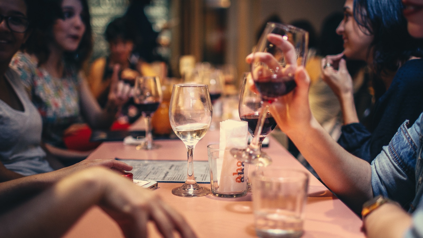 A social table with wine glasses, an empty glass and friends talking in the background